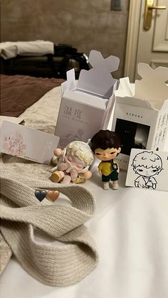 two figurines sitting on top of a bed next to boxes and other items