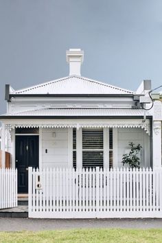 a white house with a black door and picket fence in front of it on a cloudy day