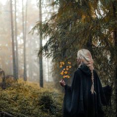 a woman standing in the woods with her back to the camera and looking at leaves