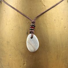 Beach pebble necklace, beige striped raw stone pendant, rock jewellery, brown cotton cord, beach found rock to wear I found this pebble on the beach in Cornwall and hung it on a brown cotton cord. The pebble is beige colour and has a faint stripes running through it I have drilled the pebble and hung it on a knotted adjustable natural coloured cotton cord  with a narrow red glass bead and two narrow bronze beads  The pebble measures approximately 27mm tall, 19mm wide and 5mm thick, the over all Beachy Necklaces, Woodland Elves, Sea Glass Diy, Children's Theatre, Pebble Pendant, Pebble Necklace, Boho Style Necklaces, Beach Stuff, Glass Diy