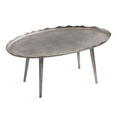 an oval metal tray sitting on top of a wooden table with two legs and a scalloped edge