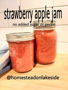 two jars filled with strawberry apple jam sitting on top of a wooden table next to a blue and white towel