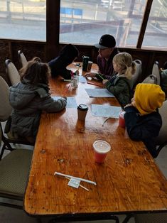 three children sitting at a table with paper on it