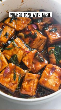 tofu with basil in a white bowl on top of a wooden table and the words braised tofu with basil above it