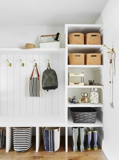 an organized closet with white shelving and storage bins, striped tote bags and rubber boots