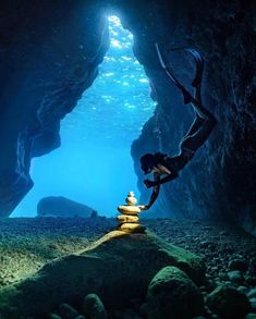 a person standing in the middle of a cave with rocks and water around them, looking up into the sky