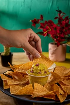 a person dipping guacamole into a bowl of salsa surrounded by tortilla chips