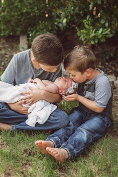 two boys are sitting on the grass and one boy is holding a baby