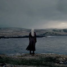 a man standing on top of a rock next to the ocean under a cloudy sky