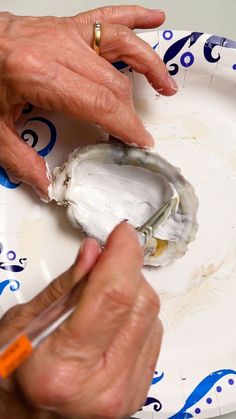 an older woman is painting a plate with blue and white designs