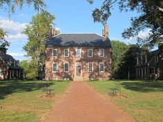 an old brick house with trees in the front yard and walkway leading to it on a sunny day