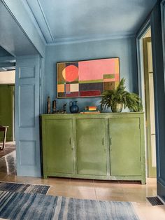 a living room with blue walls and green cabinet in the center, rug on the floor