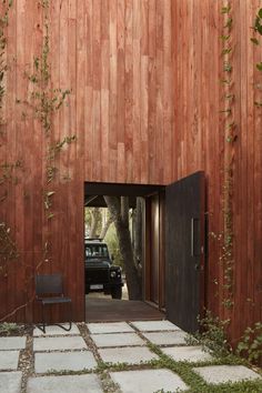 a black car is parked in front of a wooden building with an open door that leads into the yard