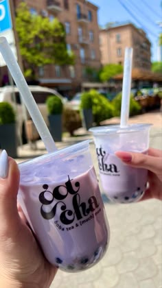 two people holding up ice cream cups with straws in their hands on a city street