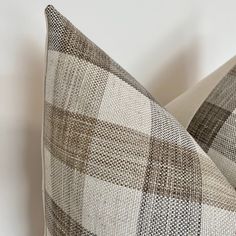 two pillows sitting next to each other on top of a white bedding set with brown and tan plaid patterns