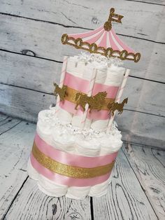 a three tiered cake with pink and gold trimmings, topped with a carousel topper