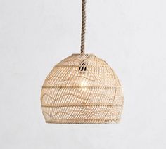 a rattan light hanging from a rope on a white wall in an empty room