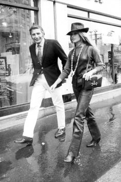 black and white photograph of two people walking down the street in front of a store