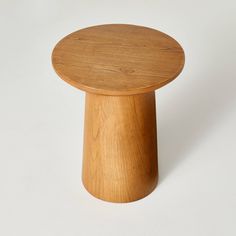 a small wooden table with a white background in the back ground and one round wood object on top