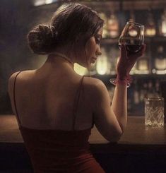 a woman sitting at a bar with a glass of wine in her hand and looking into the distance