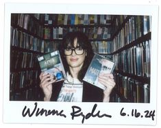 a woman holding up two dvds in front of a book shelf