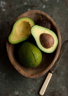 an avocado in a wooden bowl next to a knife