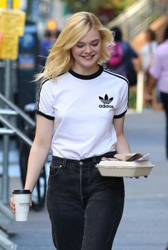 a woman walking down the street carrying a box and a coffee cup in her hand