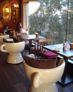 two women sitting at tables in a restaurant with large windows looking out on the trees