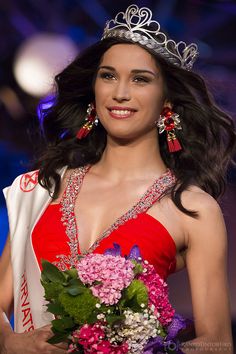 a beautiful young lady in a red dress holding a bouquet and wearing a tiara