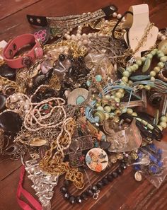 a pile of assorted necklaces and bracelets on a wooden table with other jewelry