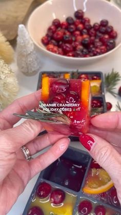 two hands holding small pieces of fruit in front of a bowl of cranberries