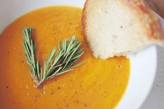 a white bowl filled with carrot soup and a piece of bread on top of it