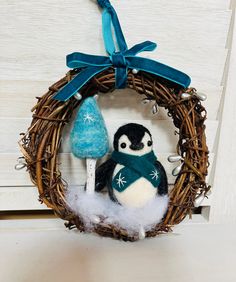 a small penguin in a wreath with a blue ribbon hanging from it's side