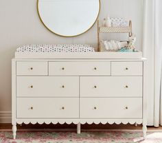 a white dresser with a mirror above it and a baby crib in the background