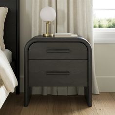 a nightstand with a lamp on top of it next to a bed