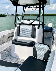 the inside of a white boat with black seats on it's front deck and water in the background