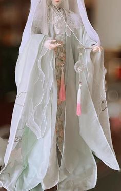 a doll is dressed in white and has a veil over her head, with a pink tassel hanging from it's neck