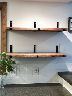 two wooden shelves are on the wall near a plant in a vase and a clock