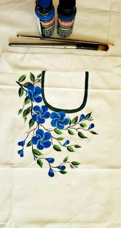 a white bag with blue flowers painted on it next to some paintbrushes and glue