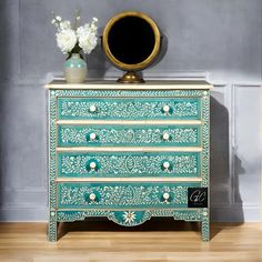 a green and gold painted dresser with flowers in vase next to it on wooden floor