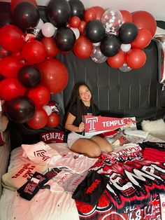 a woman sitting on top of a bed with red and black balloons hanging from the ceiling