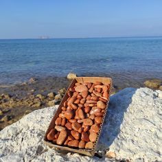 a box filled with rocks sitting on top of a rock next to the ocean's edge