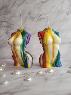 two colorful candles sitting next to each other on a marble surface with pearls around them