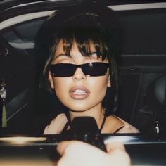 a woman wearing sunglasses and holding a cell phone in her hand while sitting in the back seat of a car