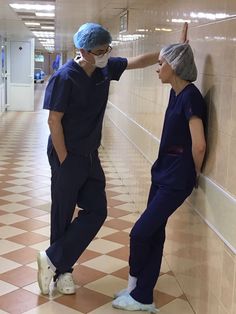 two doctors standing next to each other in scrubs on their heads and one is touching the wall