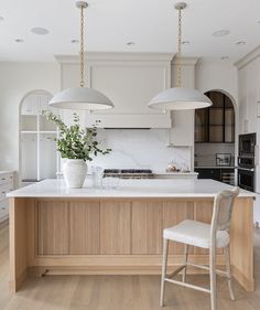 a kitchen with white cabinets and two pendant lights over the island in front of it