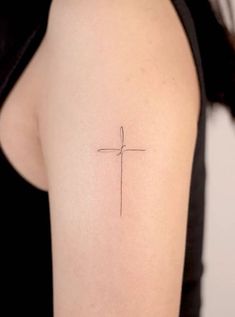 a small cross tattoo on the back of a woman's left upper half arm