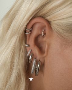 a woman with blonde hair wearing three silver rings and two star ear cuff earrings on her left ear