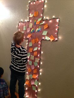 a young boy standing in front of a cross made out of post - it notes