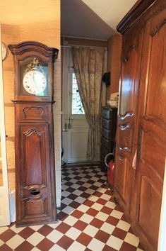 an old wooden grandfather clock sitting in the corner of a room with checkered flooring